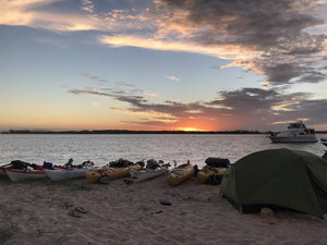 Luxe Habitat tent set up beside a row of kayaks on beach at sunset