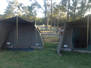 Two canvas safari tents pitched side-by-side at campsite with horse in background