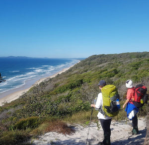 Two female hikers wearing packs at the top of a hill looking out towards the ocean