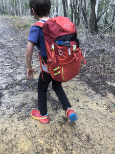 Young child wearing Osprey Jet 18 pack on walking trail surrounded by trees